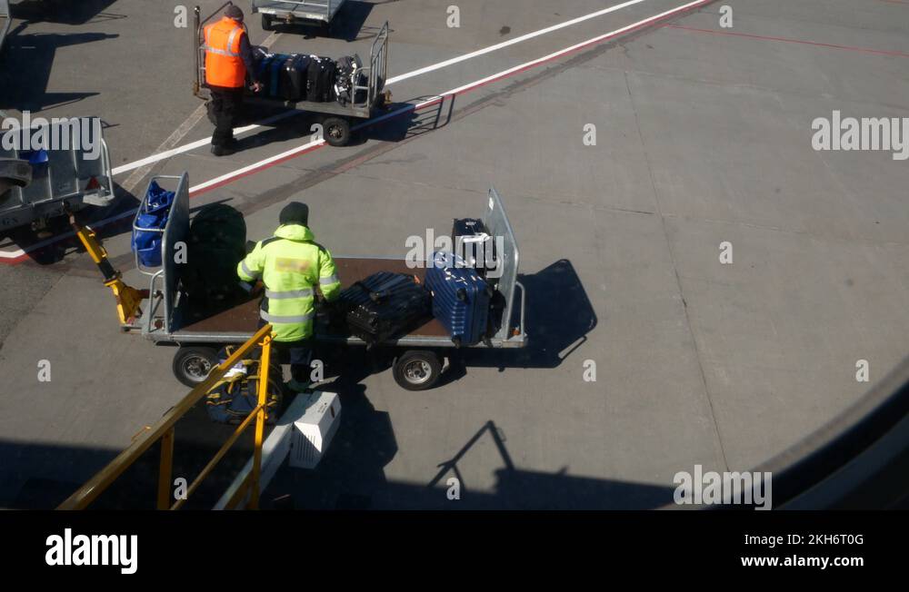 Baggage handlers check and load luggage from carts on an airport tarmac