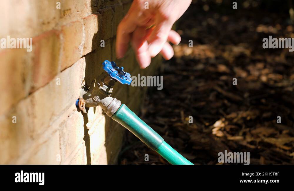 Man turning on outdoor water spigot for watering garden and lawn