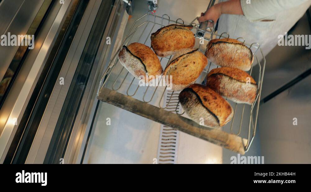 Baker pulling breads from oven and putting on shelves stacked Stock