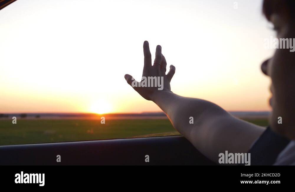 A young girl put her hand out of the car window at sunset. Close up
