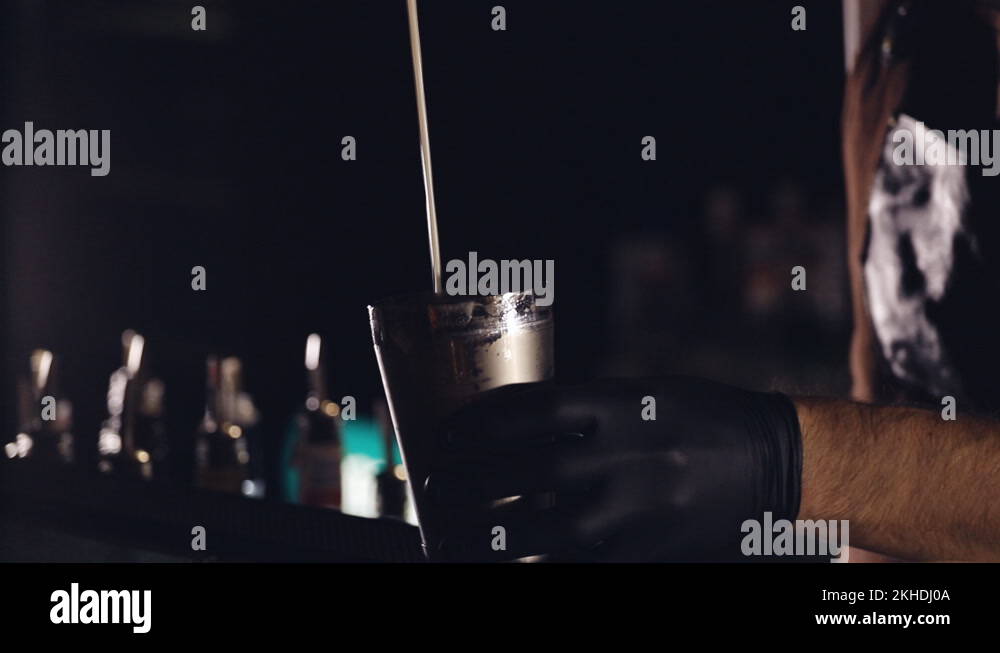 A cocktail is poured from a shaker in a bar with soft lighting. slow