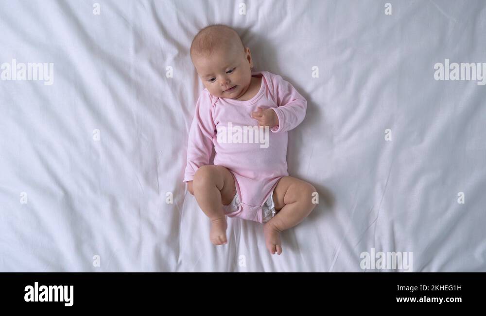 Active cute baby girl lying on bed, moving tiny arms and legs, healthy infancy Stock Video