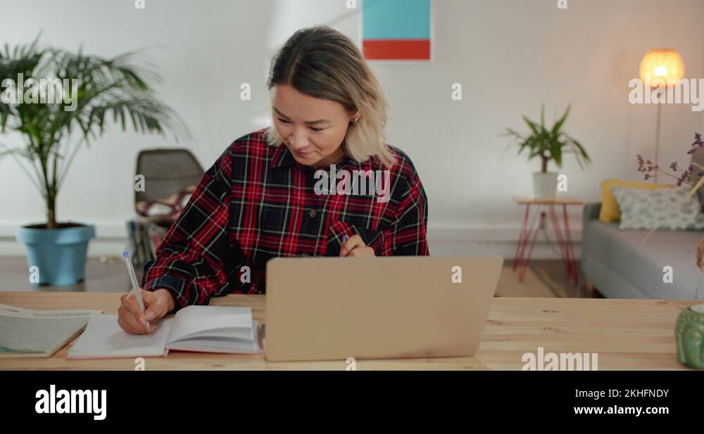 Working process of nice pensive Asian girl taking notes at modern cozy ...