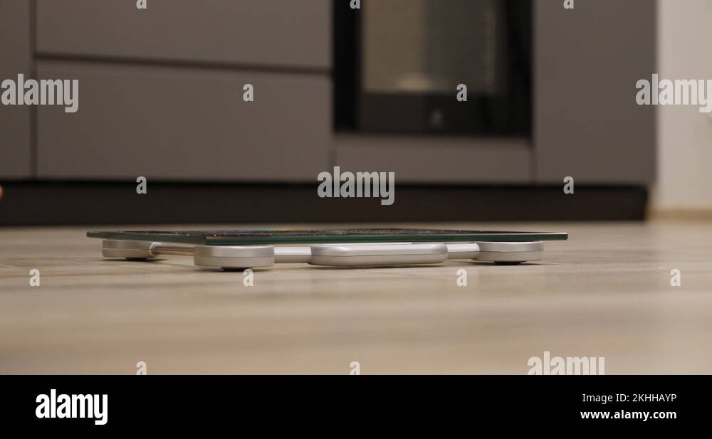 Female feet standing on weighing scales in room. Woman legs step on