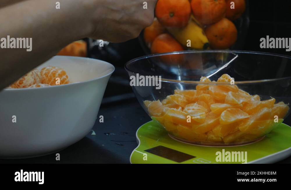 Female is measuring mandarin on scales, close up. Woman peels mandarin in Stock Video Footage