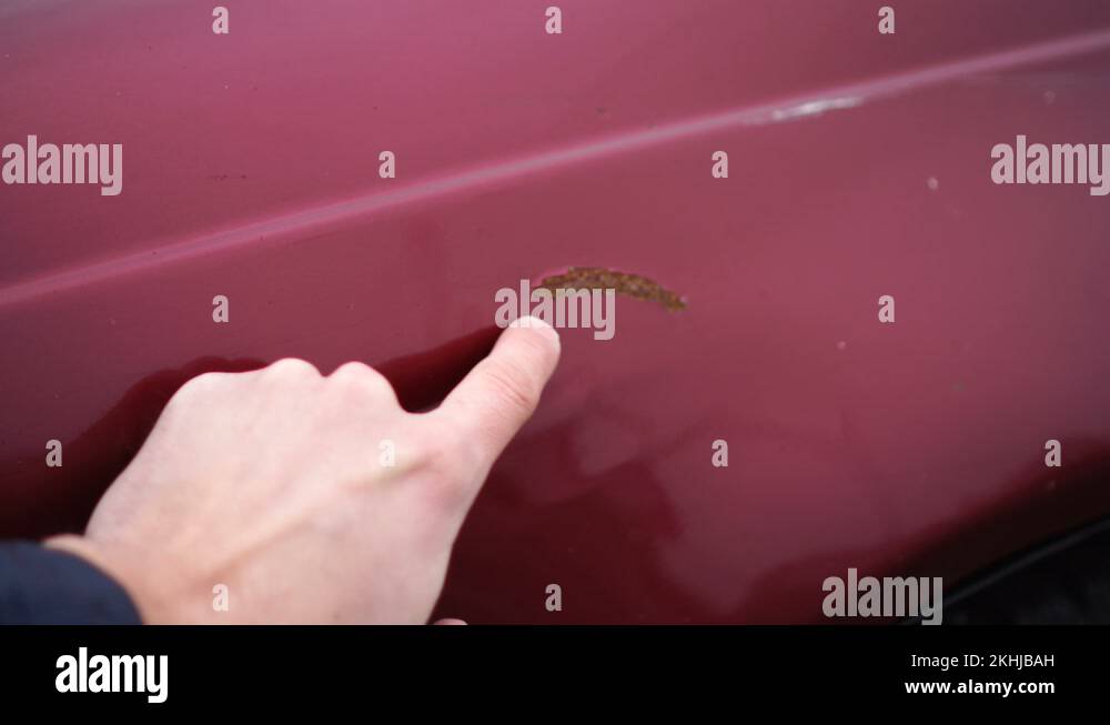 Man shows scratches with rust in a car paint. Finger show scratch on