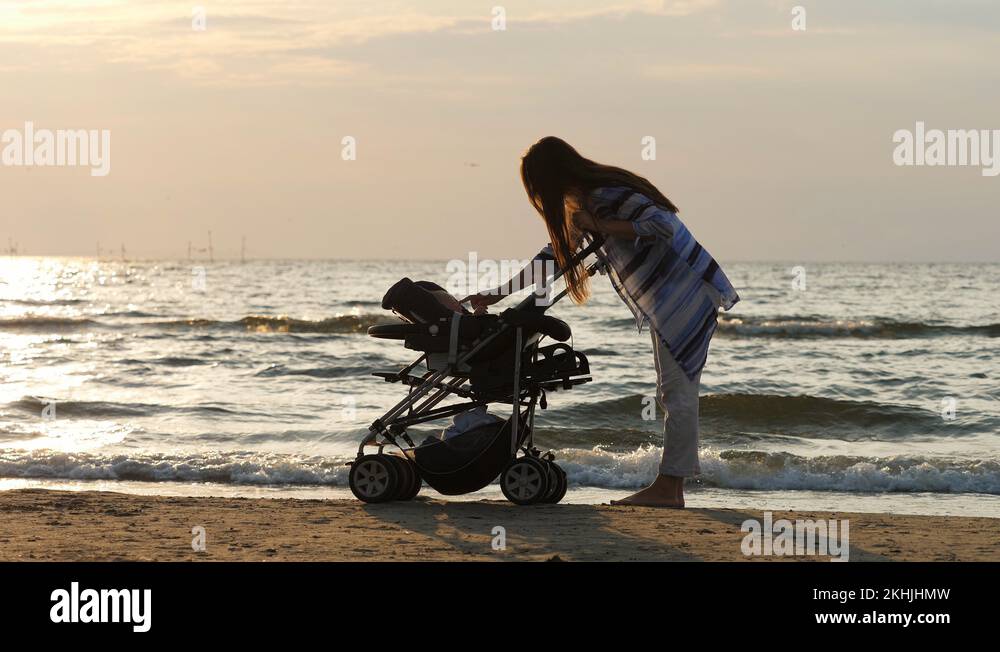 Mother play with newborn in baby cart, child moves happy hands and legs