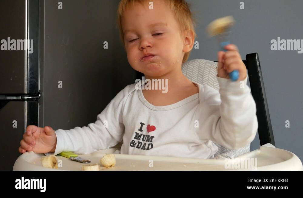 Little Adorable Blonde Boy in White Eating Banana Using Baby Fork and Knife Stock Video Footage