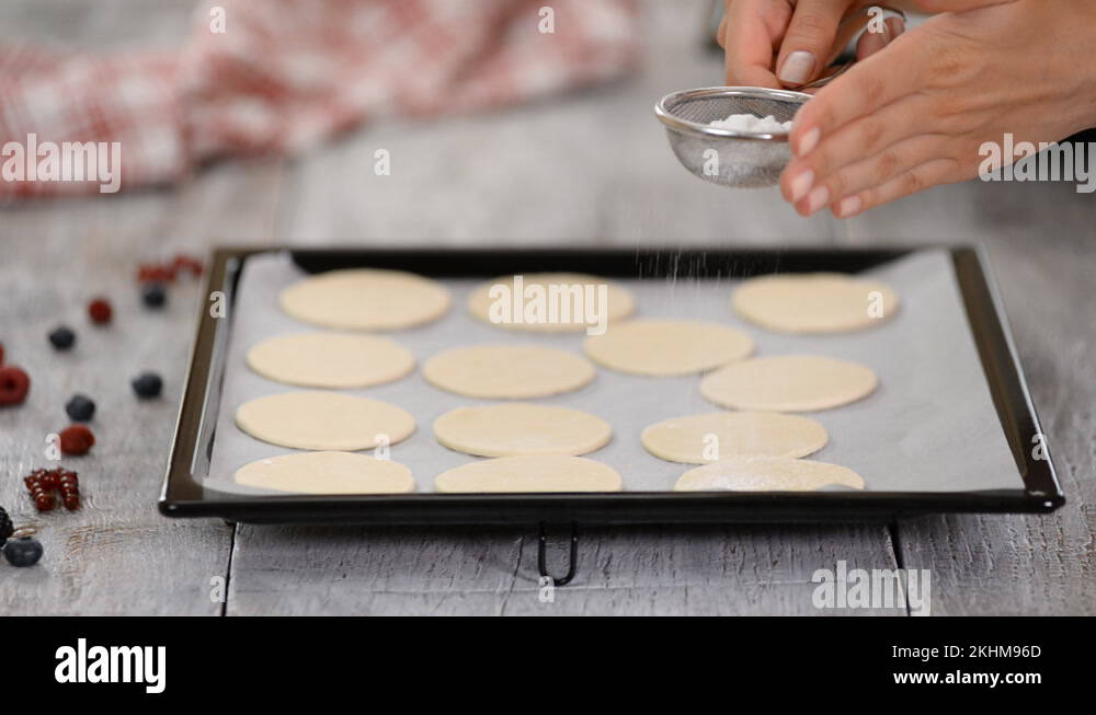 A baker uses a sifter to sprinkle powdered sugar on puff pastry. Making