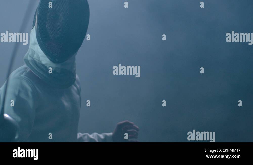 Professional fencer in uniform practicing maneuvers with sword in dark