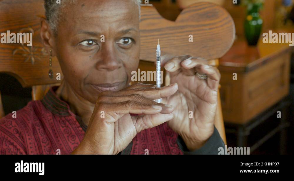 Black senior woman with a needle and syringe giving herself an ...