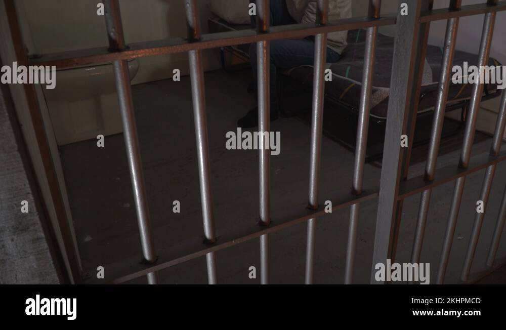 Female Prisoner behind bars in a Jail / Prison Cell. Inmate is sat on