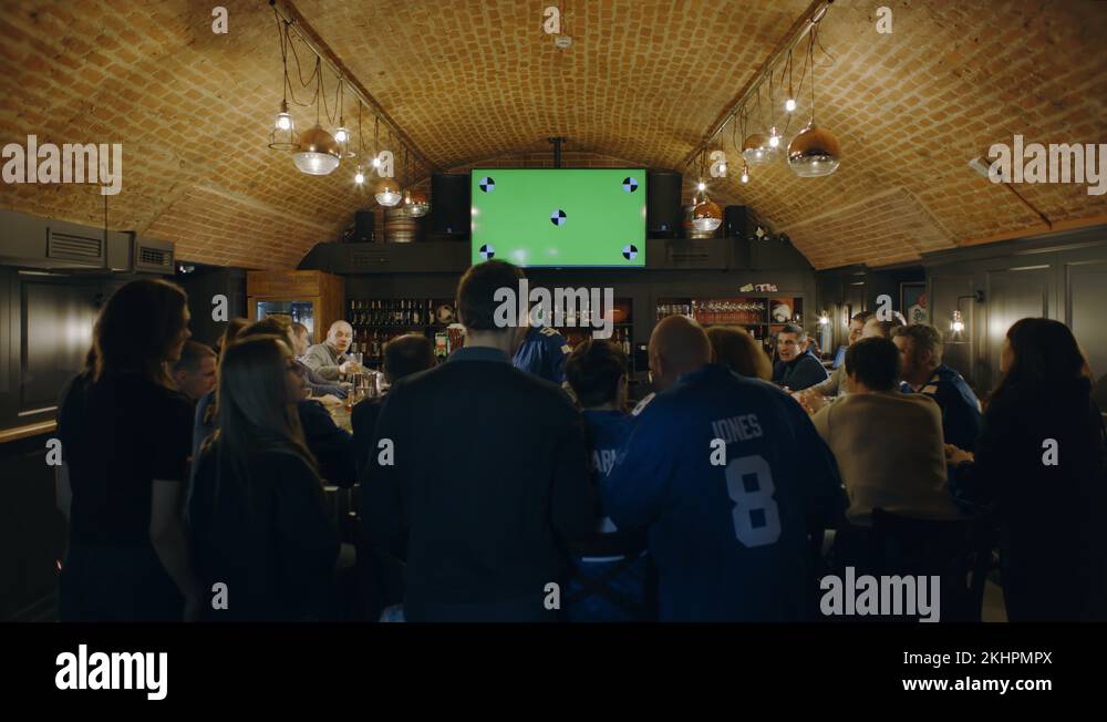Fans watching a game on a large TV in a sport pub, green screen chroma
