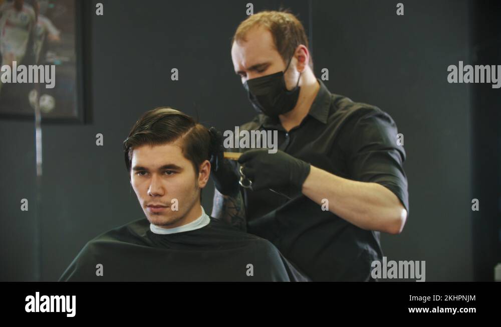 Barber cutting young man client's wet hair on the nape mirror