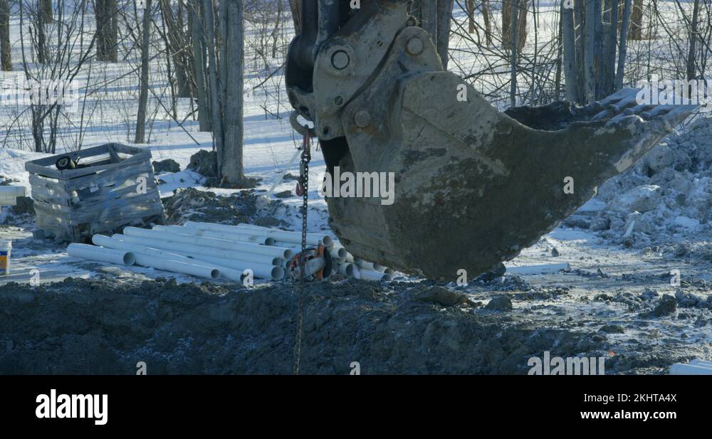 Excavator bucket with chain attached being lowered into large hole in