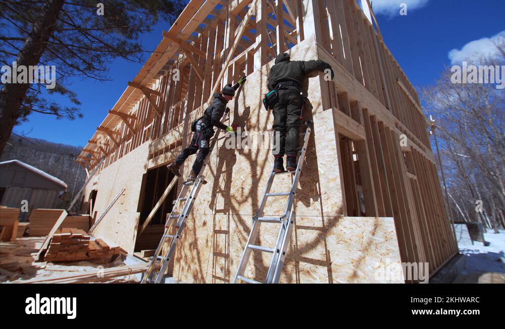 Builder on ladder nails plywoods with hydraulic hammer. Frame house ...