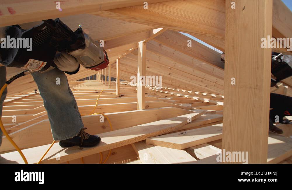 Wooden planks are nailed by builder with pnaumatic nail gun.Frame house