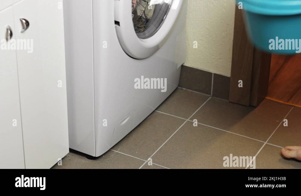 Barefoot woman placing a bucket under a washing machine before opening