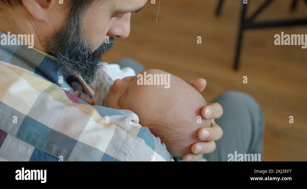 Young dad gently hugs and pats a newborn sleeping baby on head in his