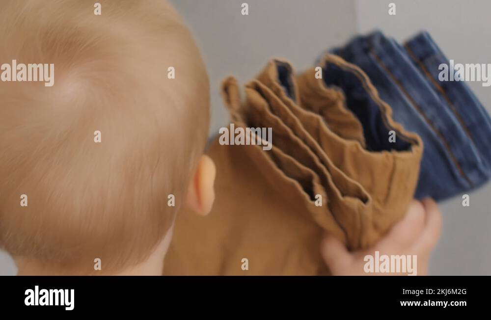Obedient cute little boy putting clothes on cupboard shelf baby help