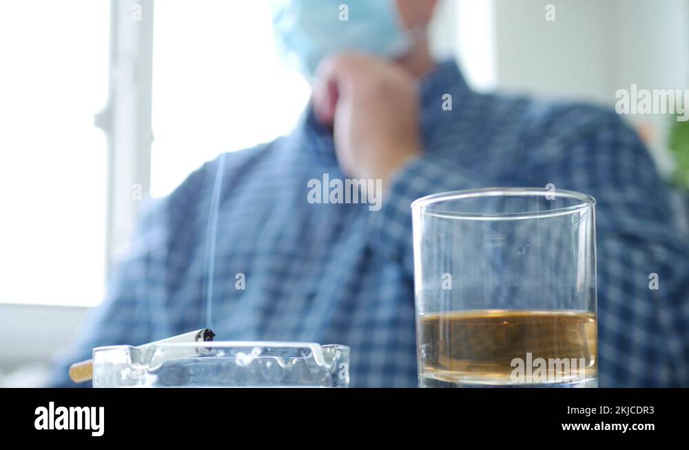 Upset Man with Protective Mask on His Face Drink Alcohol and Smoke a