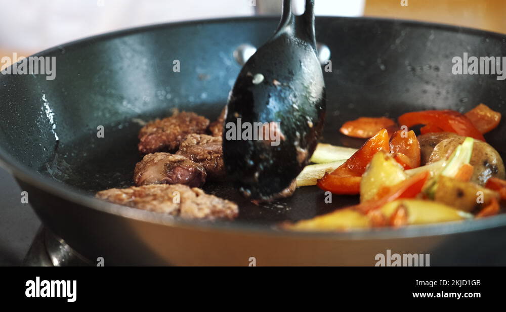 Meat and vegetables cooking frying in pan. Chef mixing food with spoon
