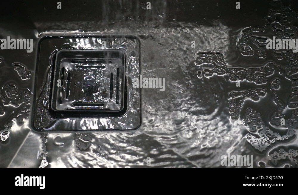 Water flows in a slow motion into a square sink of a metal sink Stock