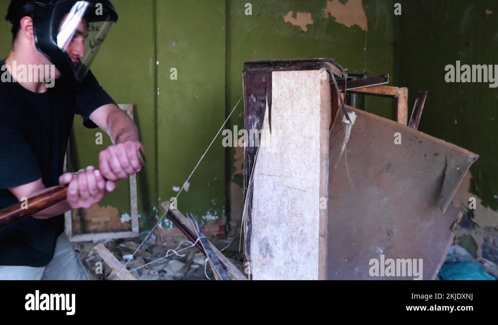 A guy smashes an old closet in an abandoned house with a baseball bat