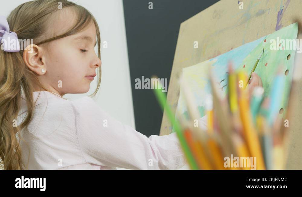 little girl paints a picture and looks at the camera. Happy little girl ...