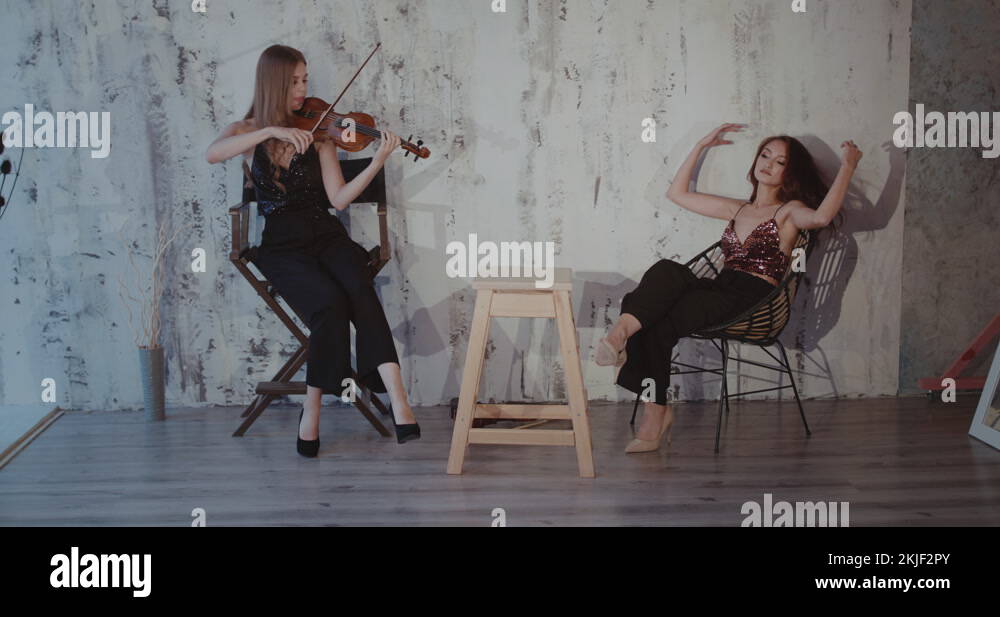 Lady throws her legs on the table and having fun while girl playing the violin Stock Video