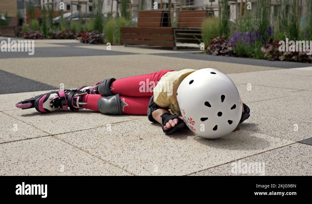 Little girl falling while roller skating. She lies on the ground in the