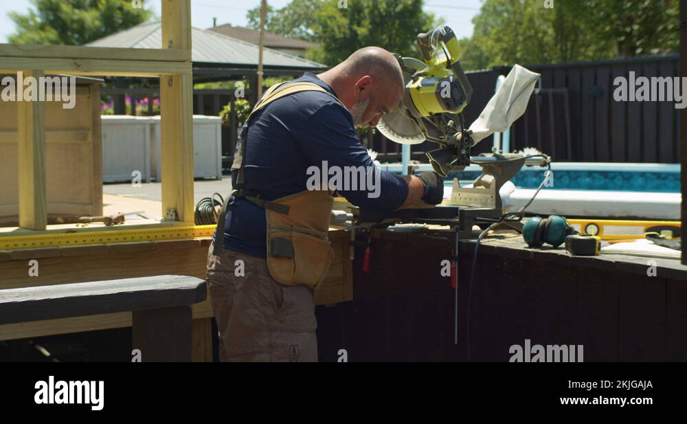 Carpenter building exterior wood deck. Using miter saw, wide shot with