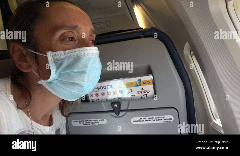 Woman wearing face mask on plane is looking out through the window