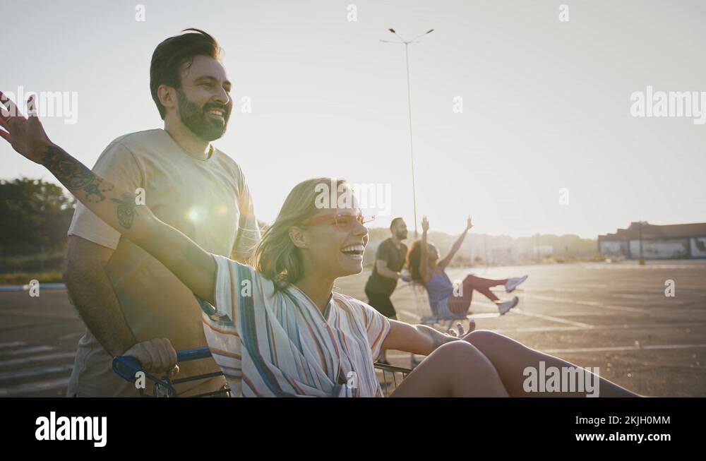 Young guys and girls riding on shopping carts at empty car parking