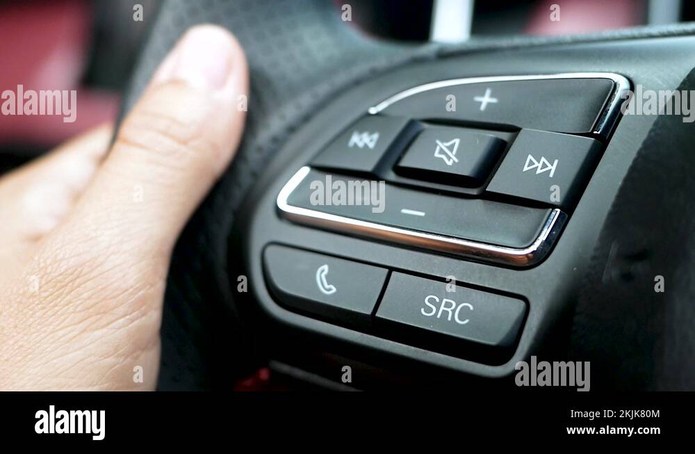 Finger pressing the audio control buttons on the steering wheel when