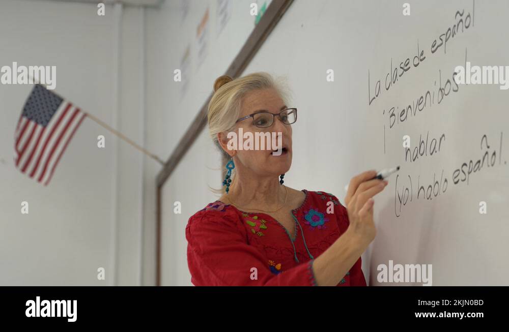Pretty blond woman teaching spanish in a school on a whiteboard with US flag Stock Video Footage
