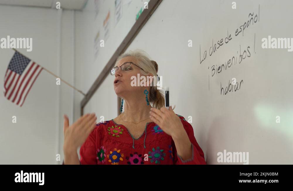 Pretty blond woman teaching spanish in a school on a whiteboard with US