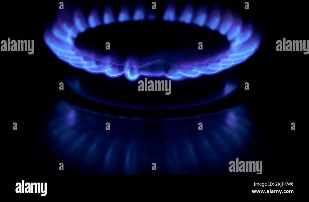 Match ignites the gas, apearing blue flame. Gas stove on black