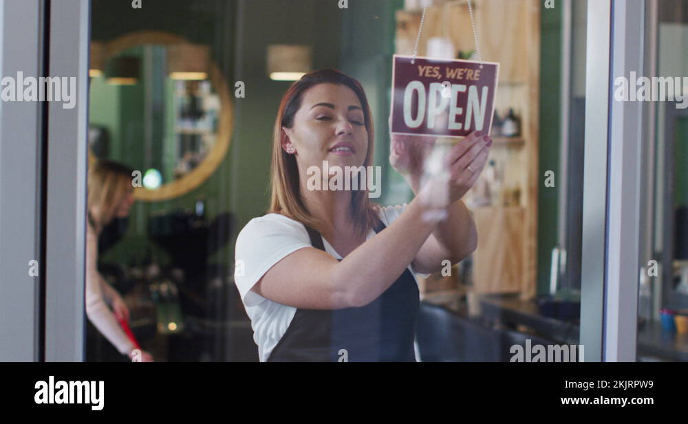 Female hairdresser changing sign board from Closed to Open at hair
