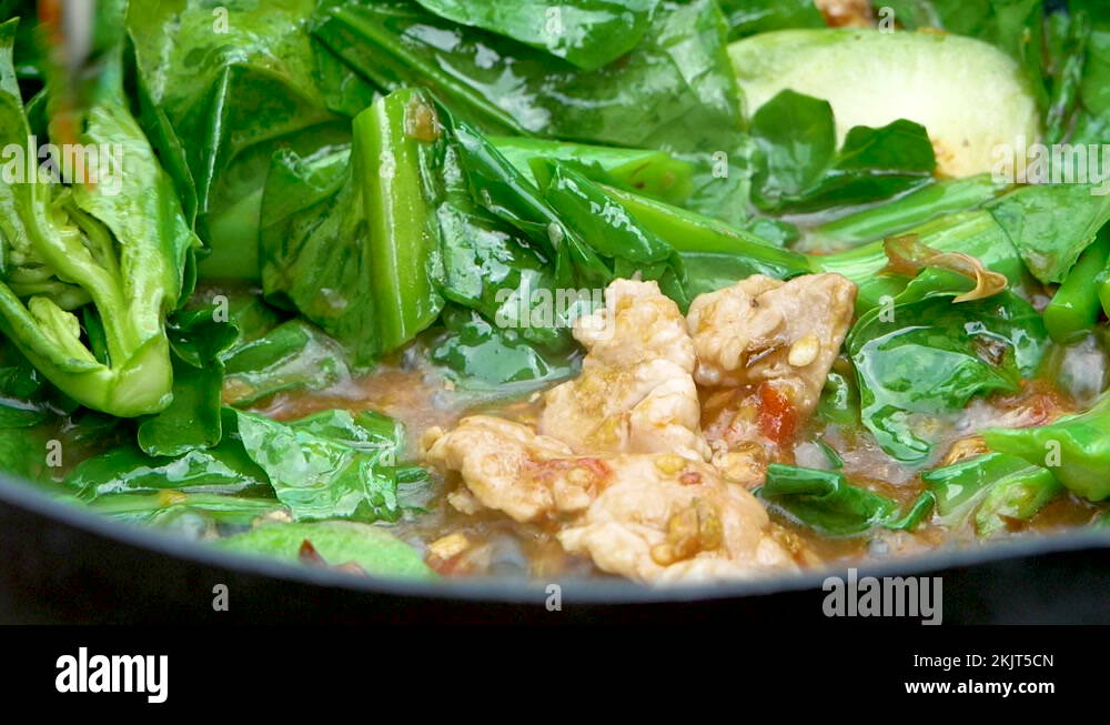 Close up of woman's hands cooking stir fried kale with pork slices in frying pan Stock Video