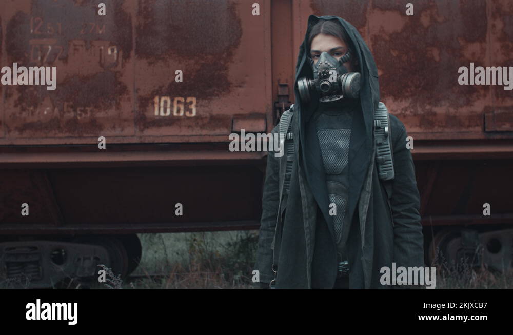Woman in grunge clothes and gas mask by rusty train carriage. Dystopian