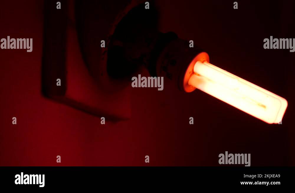 Fluorescent electric lamp glows faintly with pink light in dark room