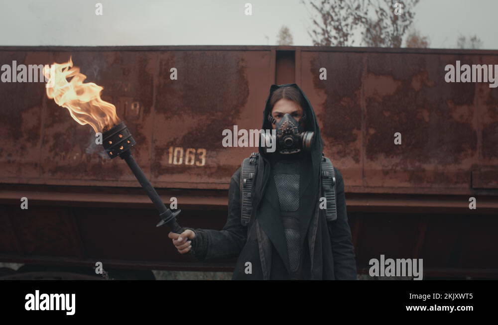 Woman in cyberpunk suit and mask hold burning torch in hand. Dystopian