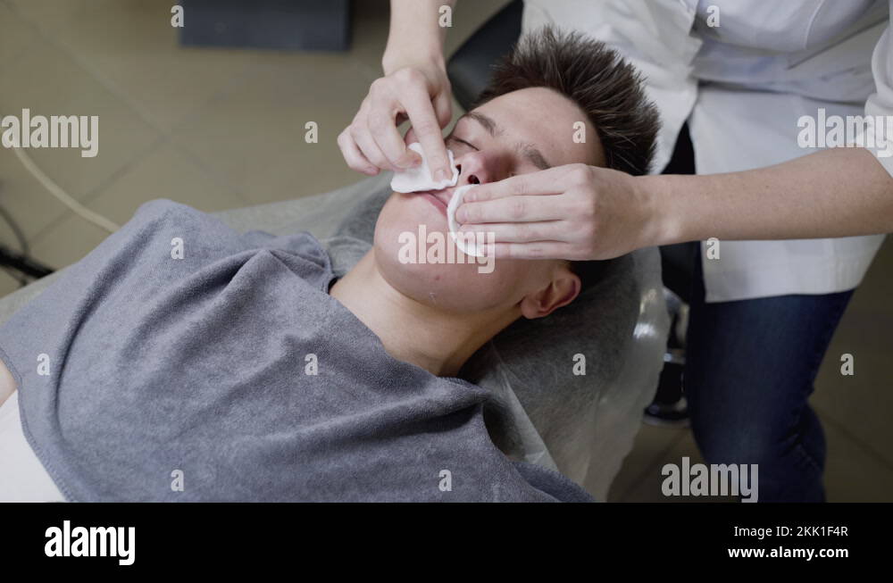 Beautician's hands wipe the man's face with cotton swabs during the
