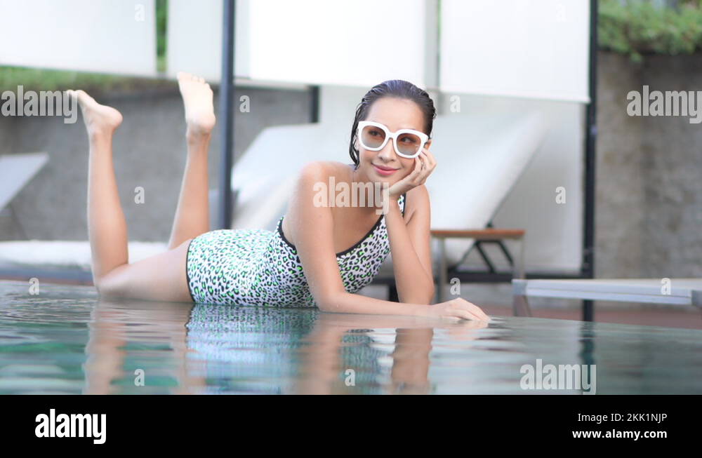 Attractive Asian woman laying on edge of swimming pool kicking feet in air Stock Video Footage
