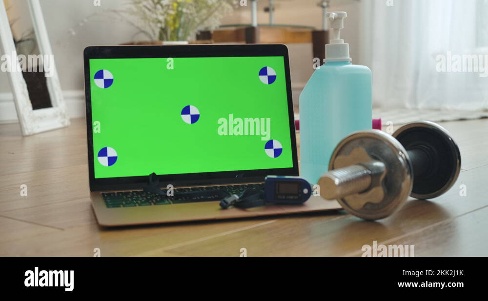 Green screen on laptop, dumbbell, pulse oximeter, and bottle of