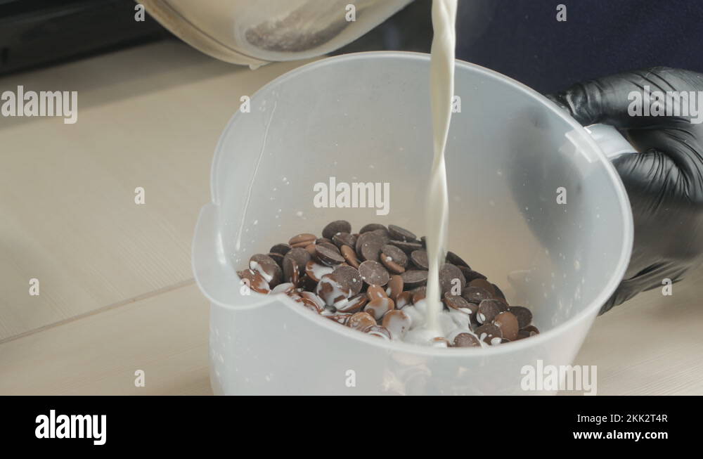 a pastry chef pours hot milk into a container with chocolate tablets