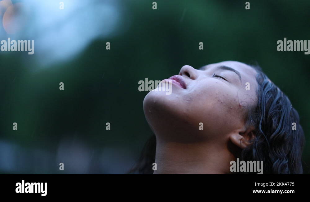 Smiling young woman in rain shower, person standing outside while