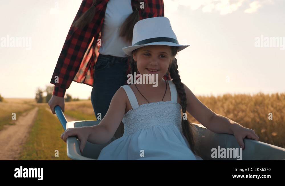 A teenage girl rides her little sister on a garden cart. Children play