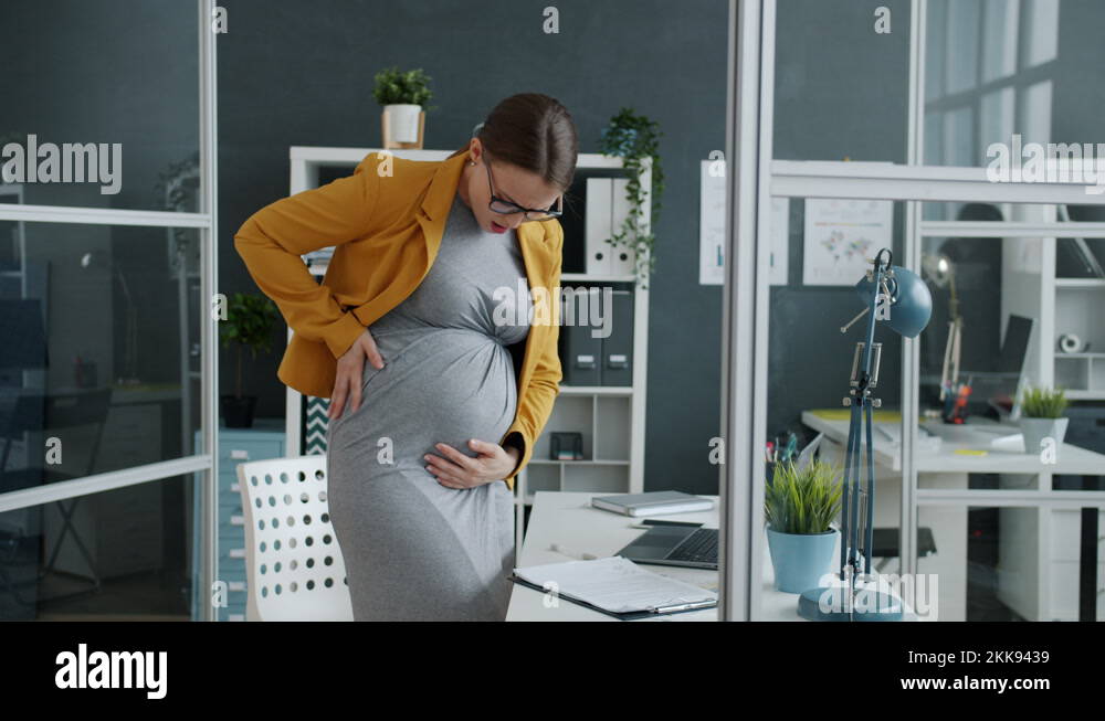 Pregnant businesswoman feeling stomach ache touching belly in workplace